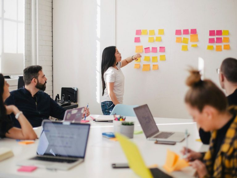 Woman presenting to team using colourful sticky notes on whiteboard in conference room.