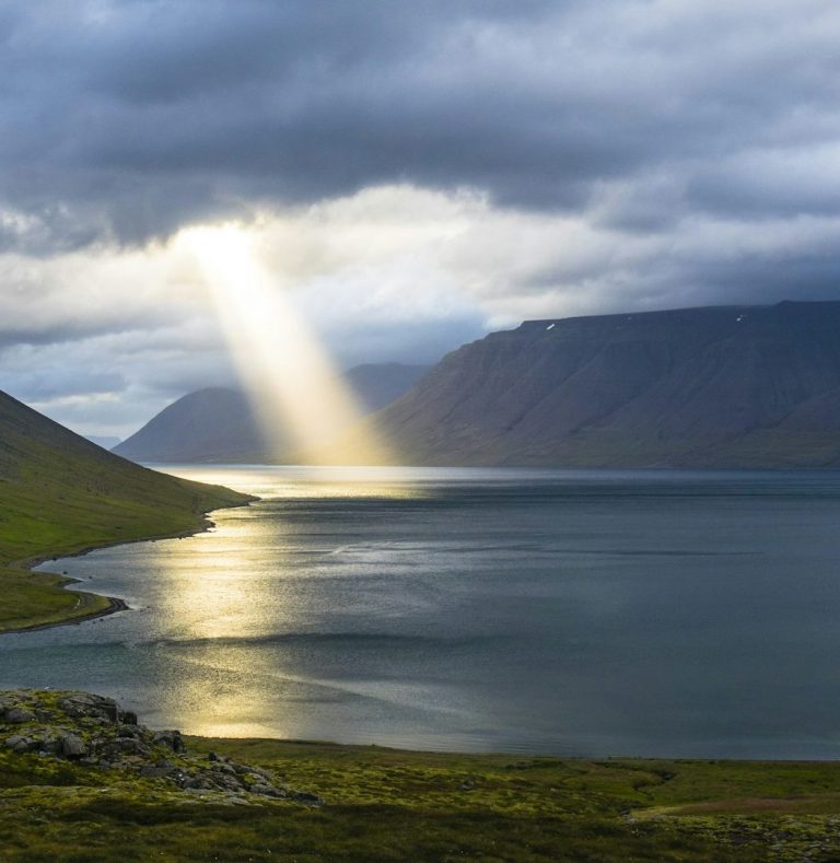 Dramatic sunbeam breaking through storm clouds over mountain lake landscape.