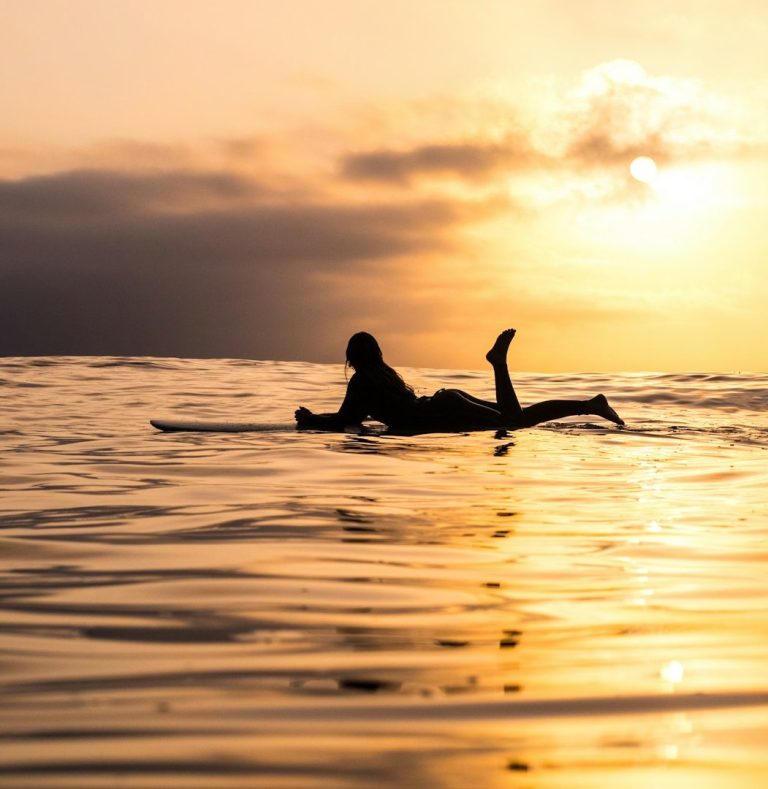 Person floating on surfboard in calm ocean water at sunset.